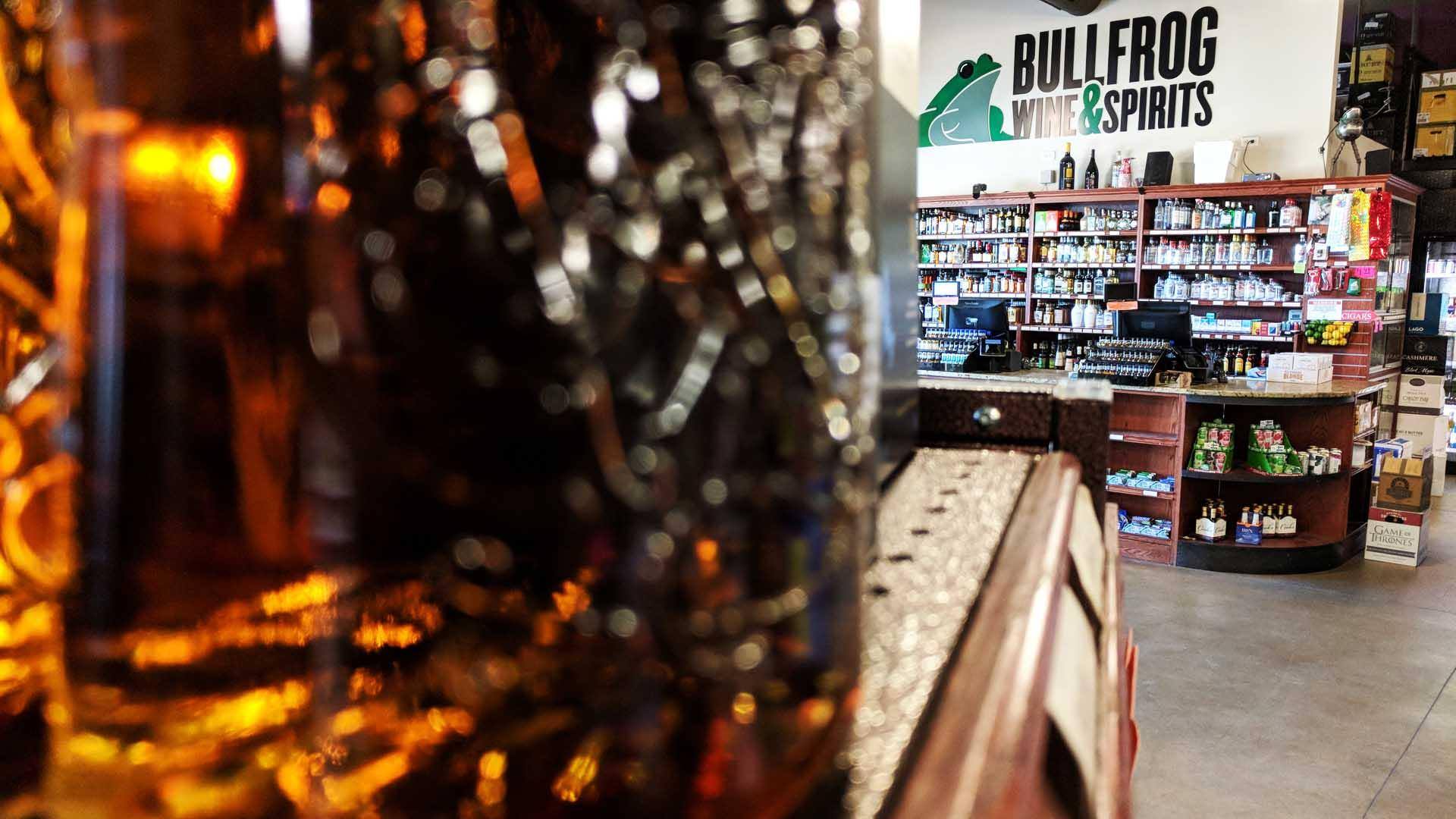 The Bullfrog Register stands in the distance behind a shelf lined with fancy liquor bottles.