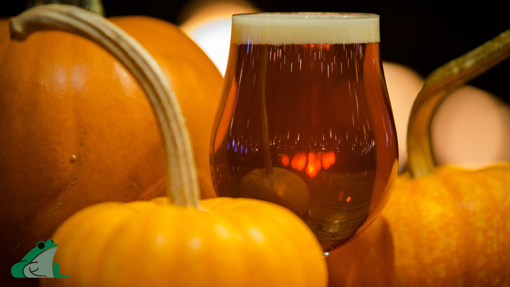Glass of pumpkin beer surrounded by fresh pumpkins, highlighting Bullfrog Wine and Spirits September seasonal specials.