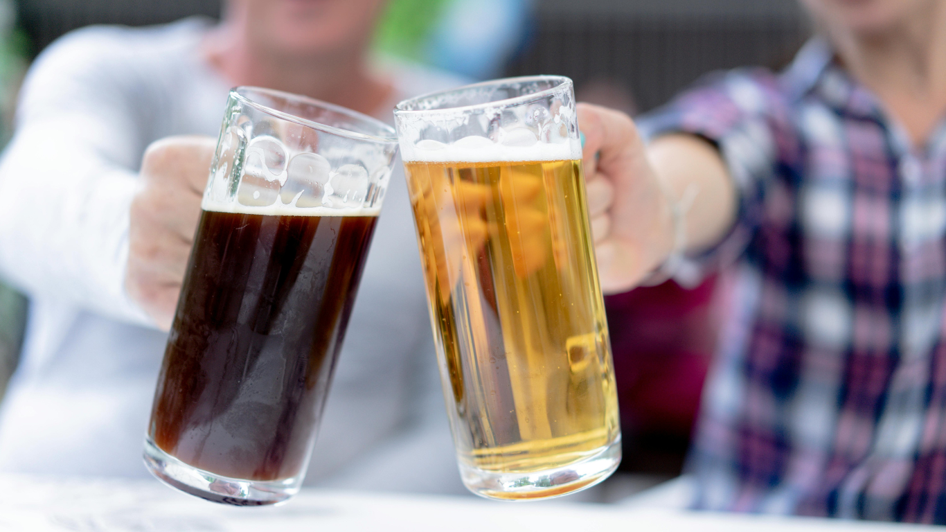 Two people clinking glasses of dark and light craft beer in celebration at an outdoor fall beer festival. Beers found at Bullfrog Wine & Spirits in Fort Collins