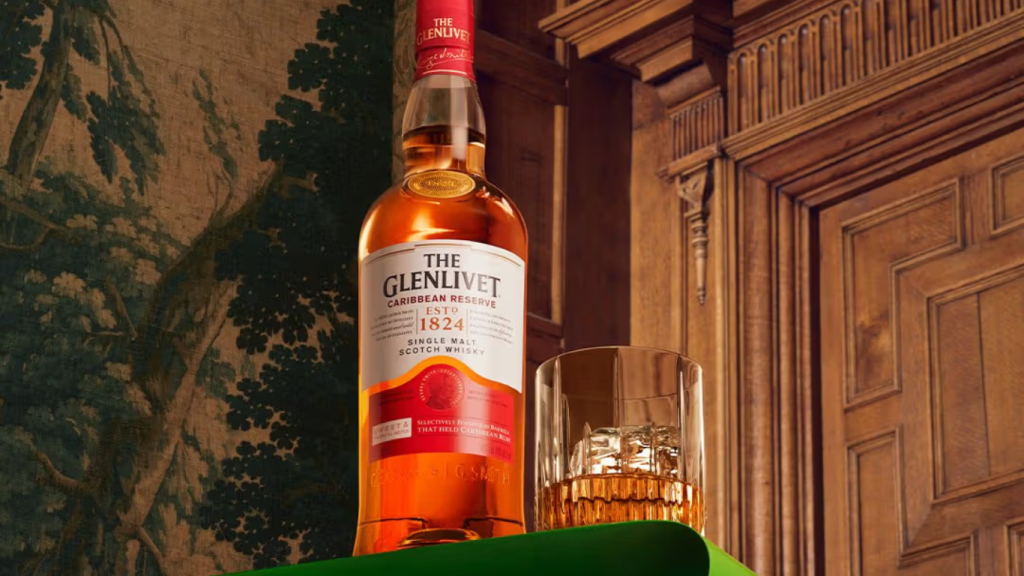 Elegant bottle of the Glenlivet Caribbean Reserve Single Malt Scotch Whisky with a glass of whisky on the rocks, set against a classic wood-paneled backdrop-ideal for luxury holiday or hostess gifting.